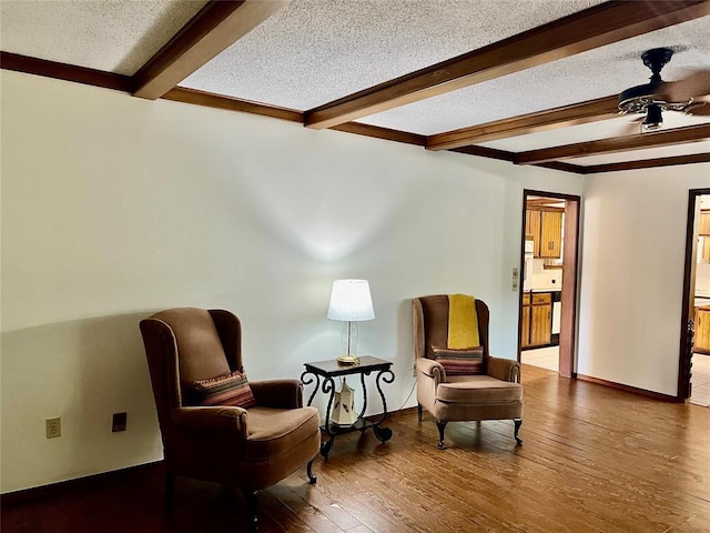 sitting room featuring beam ceiling, ceiling fan, a textured ceiling, hardwood / wood-style flooring, and baseboards