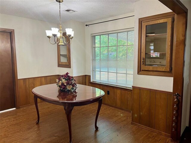 dining space with a wainscoted wall, wooden walls, a textured ceiling, a chandelier, and wood finished floors