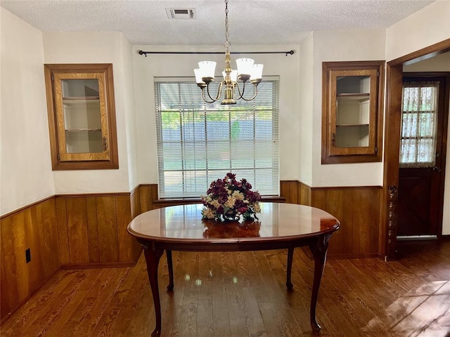 dining room with wainscoting, a chandelier, wood finished floors, a textured ceiling, and wooden walls