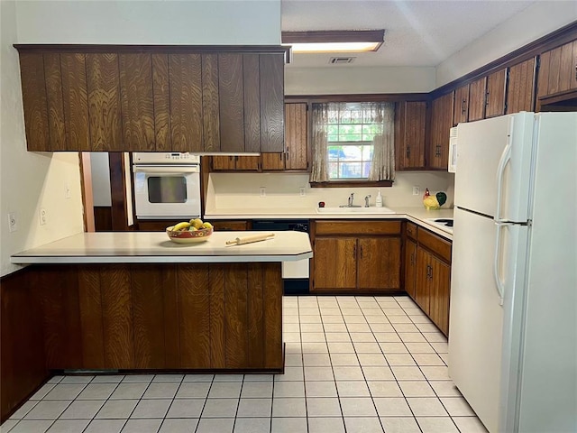 kitchen featuring white appliances, a sink, a peninsula, light countertops, and light tile patterned flooring
