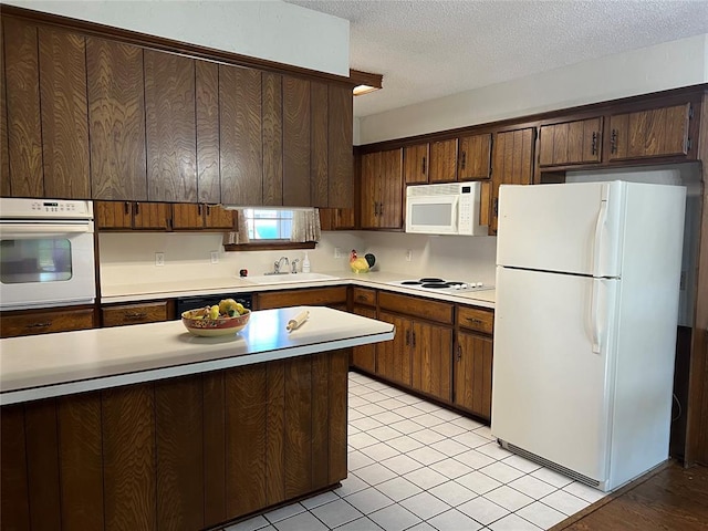 kitchen featuring white appliances, a sink, light countertops, light tile patterned floors, and a textured ceiling