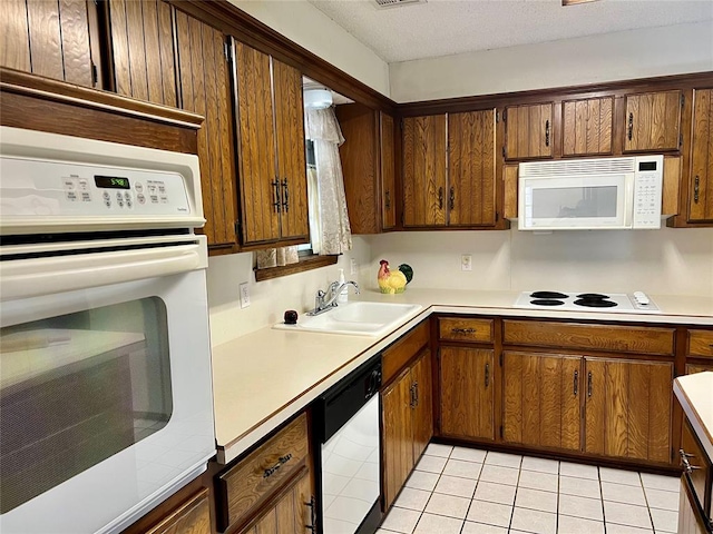 kitchen with white appliances, a sink, light countertops, light tile patterned floors, and brown cabinetry