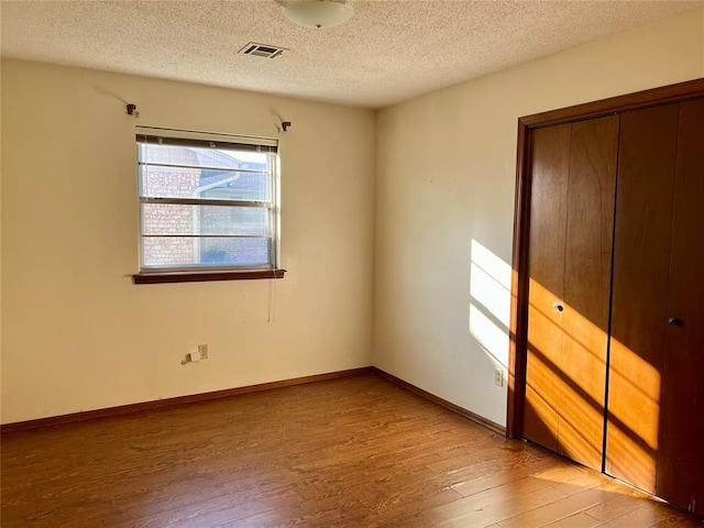 unfurnished bedroom with wood finished floors, a textured ceiling, a closet, and baseboards