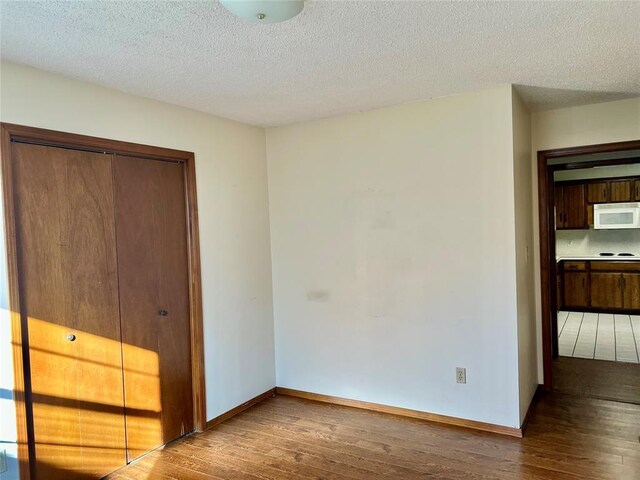 unfurnished bedroom with hardwood / wood-style flooring, a closet, baseboards, and a textured ceiling