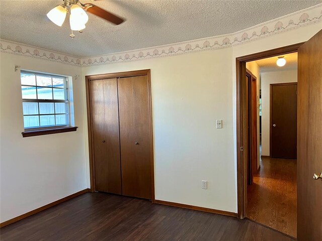 unfurnished bedroom featuring dark wood-style flooring, a textured ceiling, a closet, baseboards, and ceiling fan