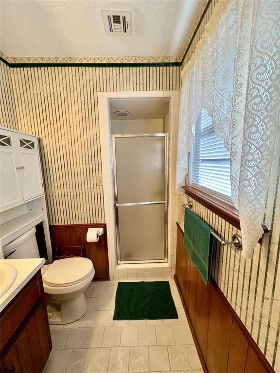 full bathroom featuring wallpapered walls, vanity, a shower stall, toilet, and tile patterned flooring