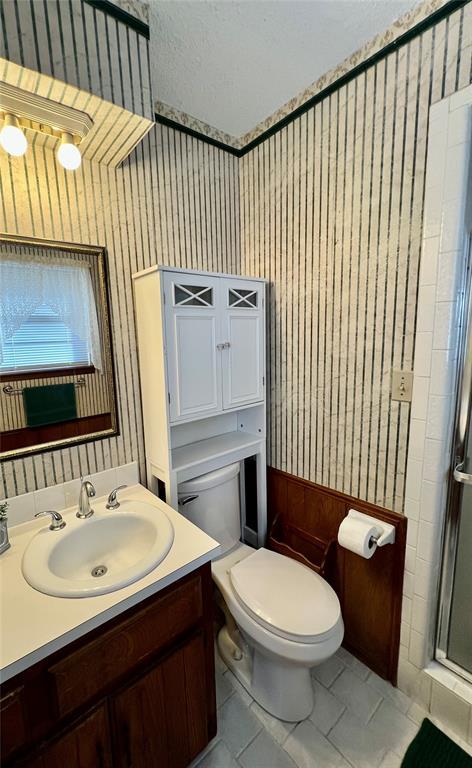 full bath with wallpapered walls, a shower stall, toilet, vanity, and tile patterned flooring
