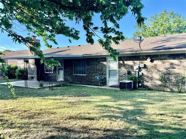 rear view of property featuring a patio area, central air condition unit, a lawn, brick siding, and a chimney