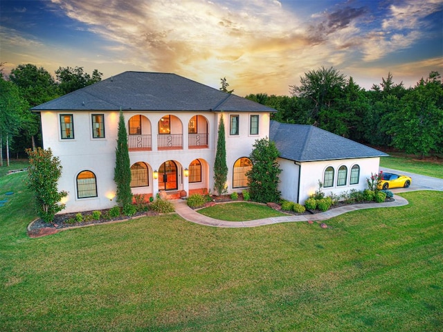 view of front of house featuring stucco siding, a shingled roof, and a front lawn
