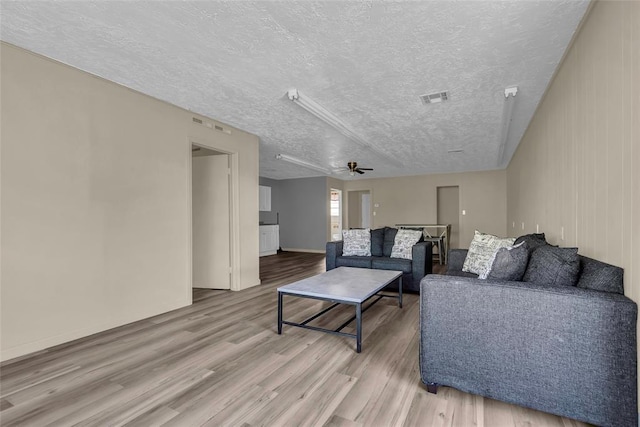living area with a ceiling fan, wood finished floors, a textured ceiling, baseboards, and visible vents