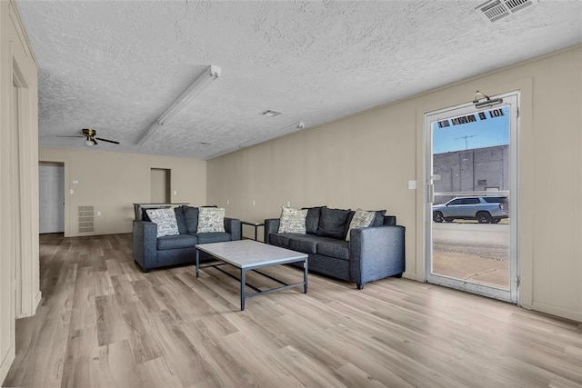 living room with a textured ceiling, light wood-style floors, and visible vents