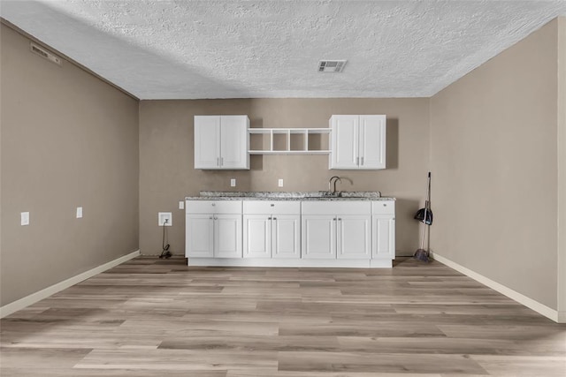clothes washing area featuring baseboards, a textured ceiling, a sink, visible vents, and light wood-style flooring