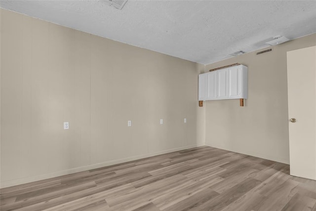 unfurnished room featuring a textured ceiling, light wood finished floors, and visible vents
