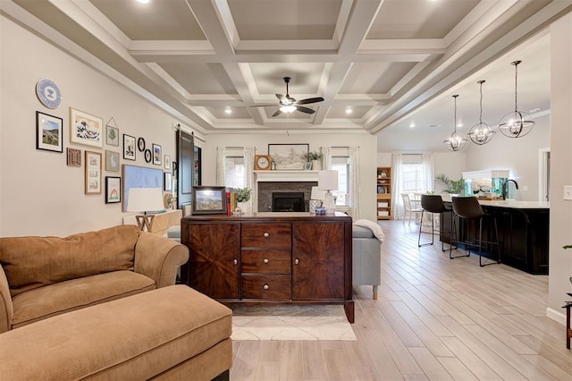 living area featuring a fireplace, beamed ceiling, light wood-type flooring, and a ceiling fan