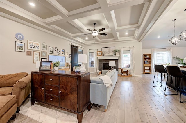 living area featuring beam ceiling, coffered ceiling, a fireplace, and ceiling fan with notable chandelier