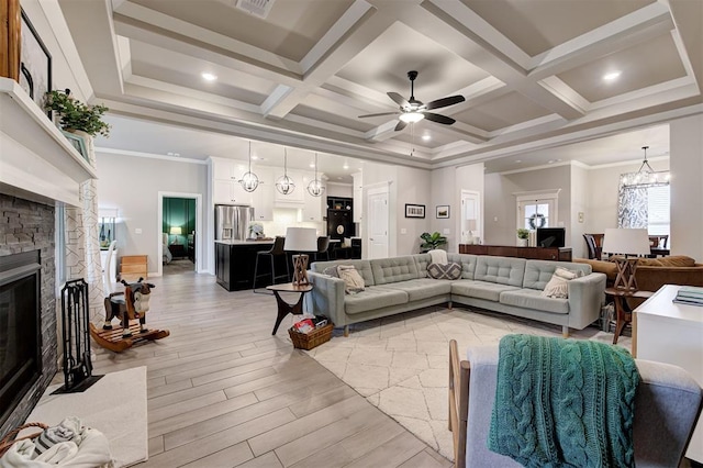 living area featuring light wood-style floors, ceiling fan with notable chandelier, beamed ceiling, and a fireplace