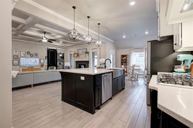 kitchen featuring light wood-style flooring, a kitchen island with sink, dark cabinetry, dishwasher, and ceiling fan with notable chandelier