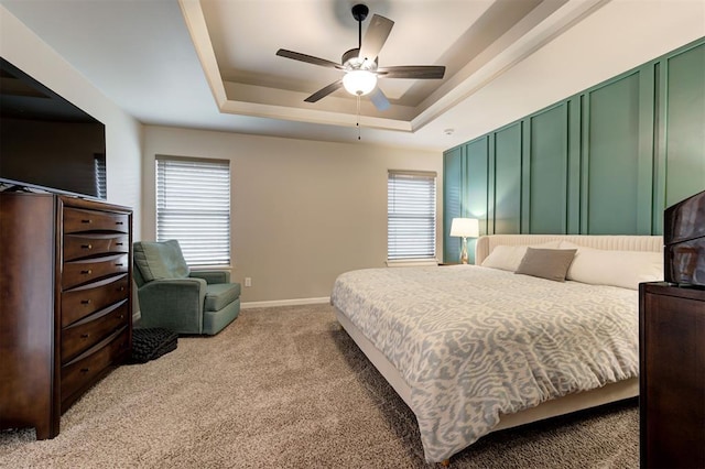 bedroom with a raised ceiling, ceiling fan, light colored carpet, and baseboards