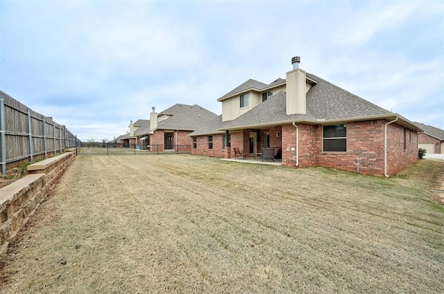 rear view of property with a patio, roof with shingles, brick siding, a fenced backyard, and a yard