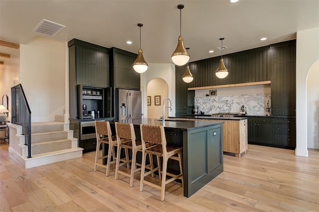 3824 Stone Hill Ln, Edmond, OK 73034 - kitchen with arched walkways, dark countertops, an island with sink, recessed lighting, and backsplash