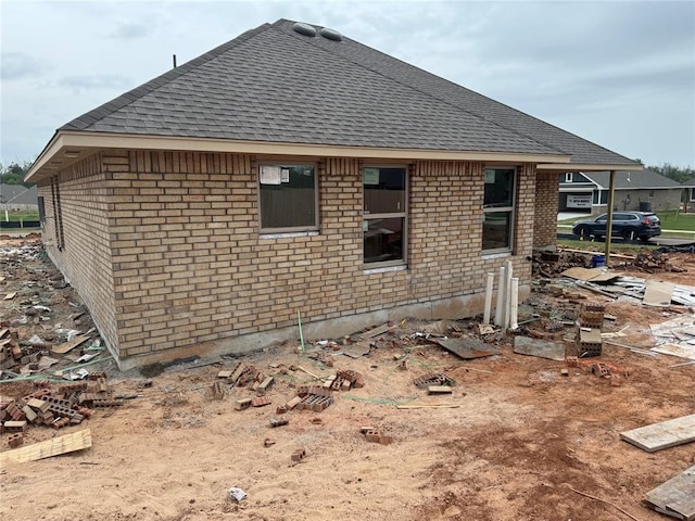 rear view of house with brick siding and roof with shingles