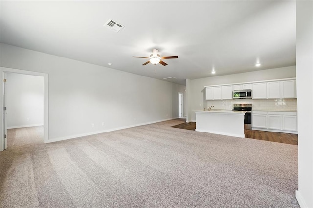 unfurnished living room featuring visible vents, a sink, baseboards, a ceiling fan, and carpet