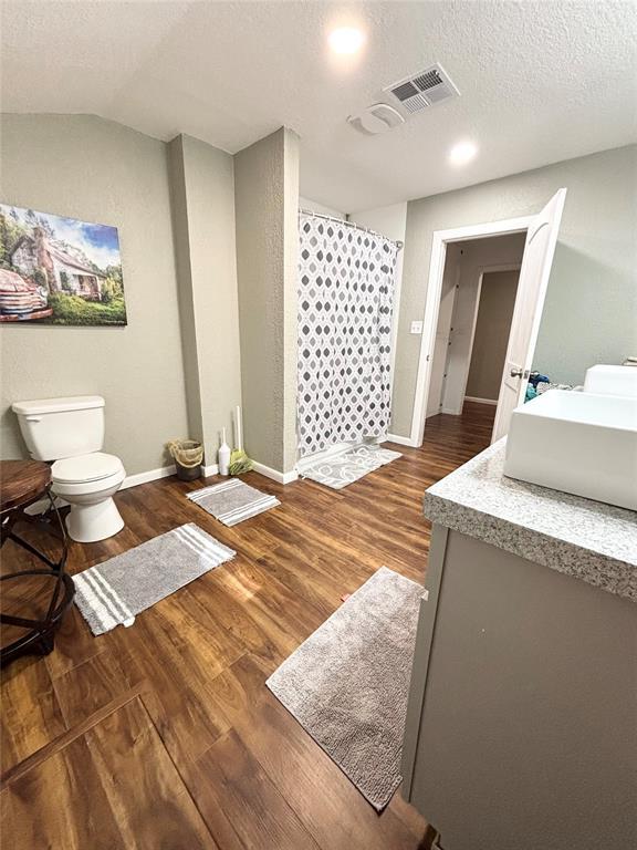 9737 NE State Highway 15, Shattuck, OK 32911 - bathroom with a shower with shower curtain, vaulted ceiling, toilet, wood finished floors, and visible vents