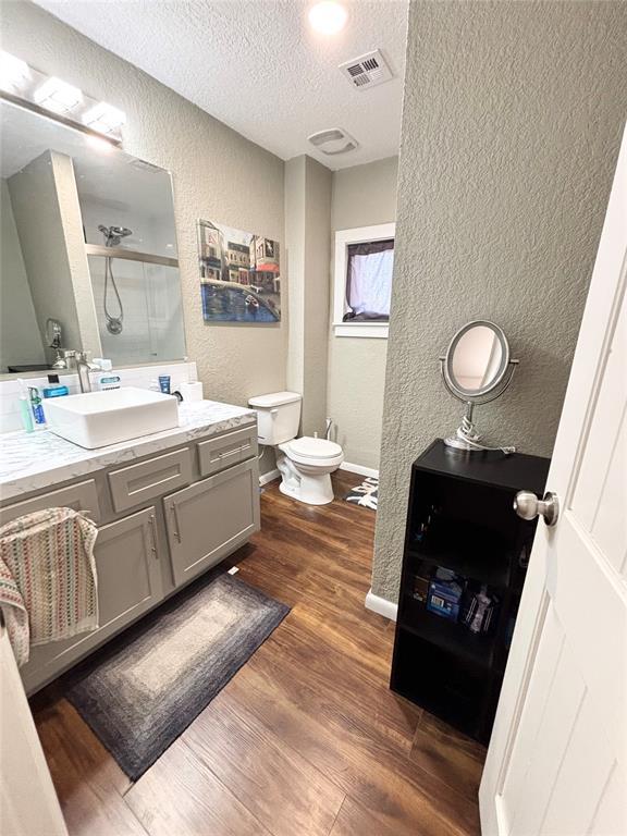 9737 NE State Highway 15, Shattuck, OK 32911 - full bath with an enclosed shower, wood finished floors, a textured ceiling, visible vents, and a textured wall