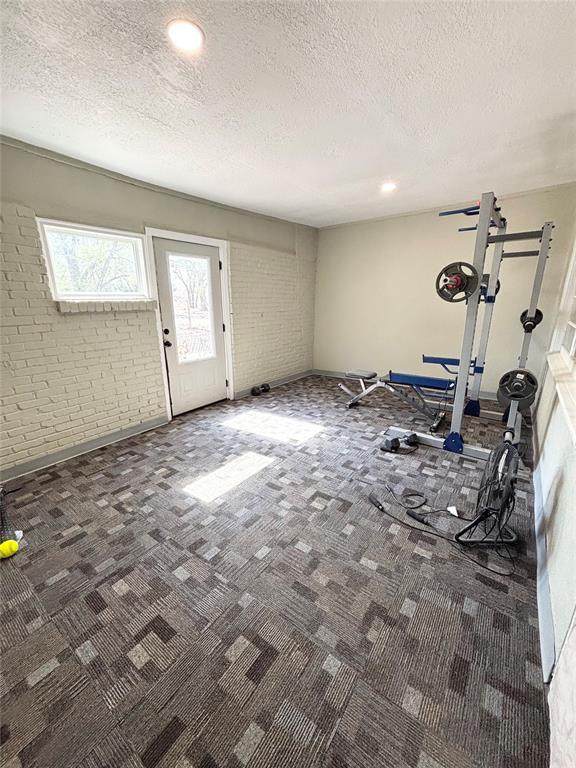 9737 NE State Highway 15, Shattuck, OK 32911 - workout room featuring brick wall, carpet flooring, and a textured ceiling