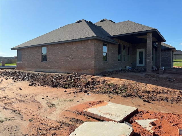 rear view of house featuring brick siding and a shingled roof