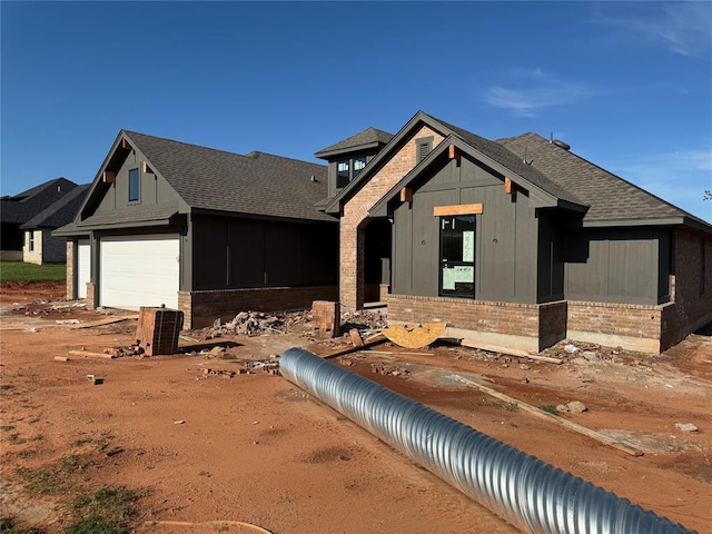 property in mid-construction featuring a garage, board and batten siding, a shingled roof, and brick siding
