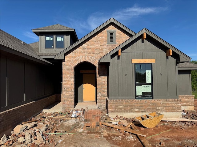 view of front of house with brick siding, board and batten siding, and roof with shingles