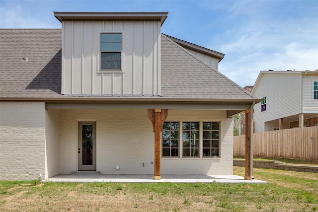 back of property featuring fence, board and batten siding, a patio, a lawn, and brick siding