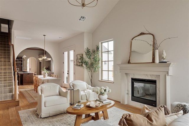 living area featuring arched walkways, a premium fireplace, light wood-style flooring, and visible vents