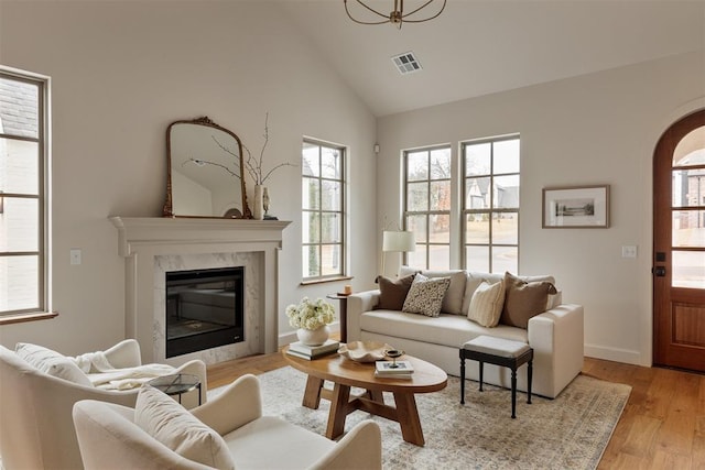 living area with light wood finished floors, a wealth of natural light, visible vents, and high vaulted ceiling