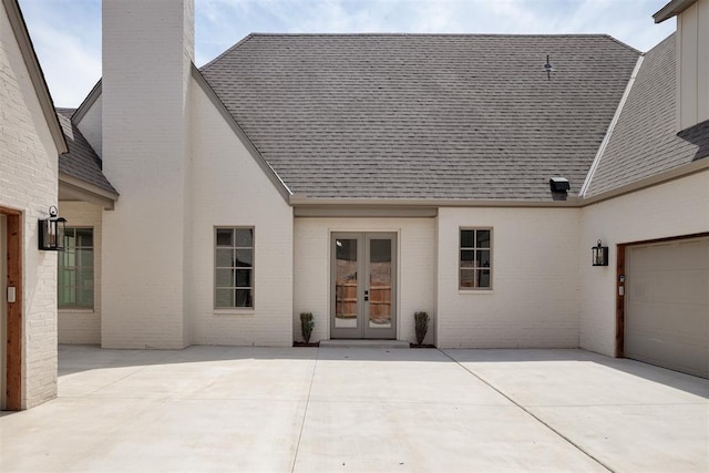 back of house featuring brick siding, french doors, a shingled roof, and a chimney