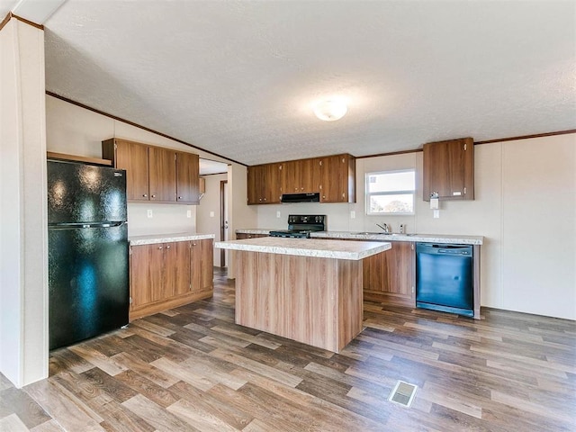 kitchen with light countertops, dark wood finished floors, under cabinet range hood, visible vents, and black appliances