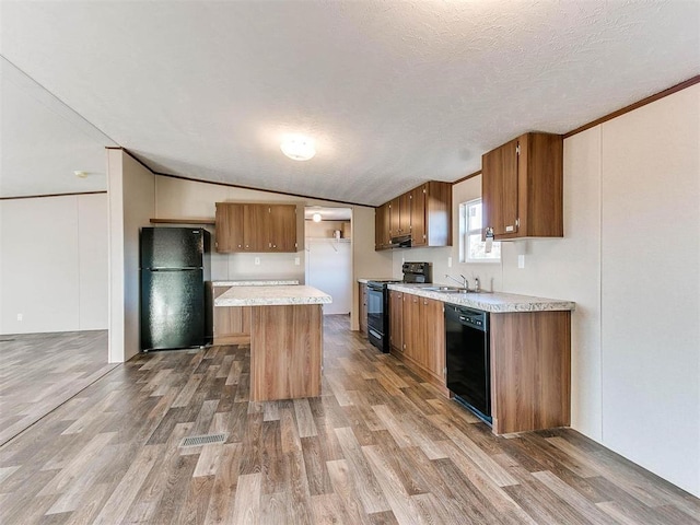 kitchen featuring a sink, black appliances, vaulted ceiling, and wood finished floors