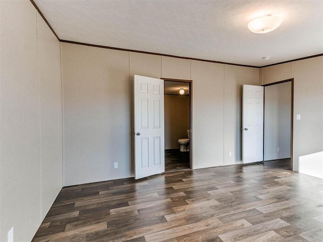 unfurnished bedroom featuring ornamental molding, ensuite bathroom, and wood finished floors