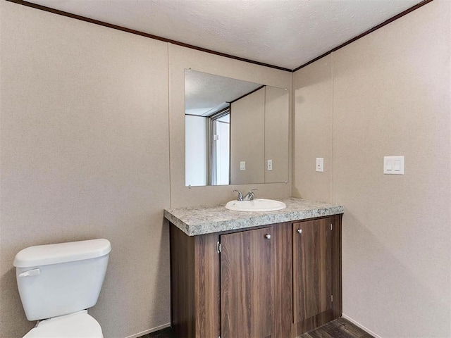 half bath featuring vanity, toilet, ornamental molding, a textured ceiling, and wood finished floors
