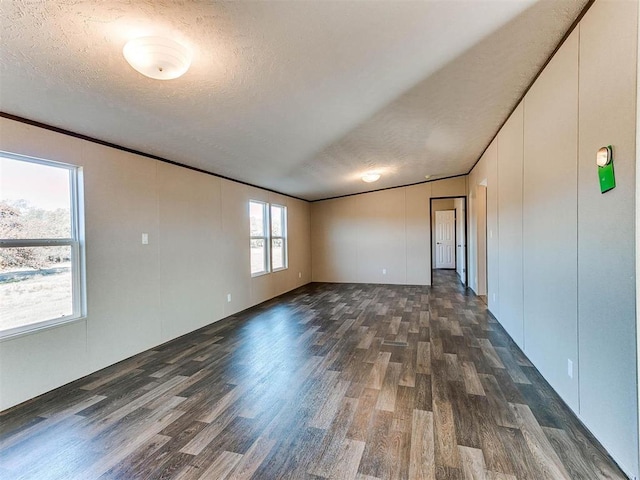 empty room with a textured ceiling, ornamental molding, and dark wood finished floors