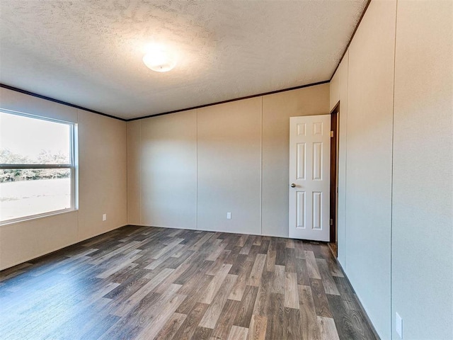 unfurnished room featuring a textured ceiling, wood finished floors, a decorative wall, and crown molding
