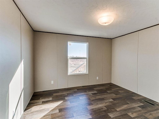 empty room featuring visible vents, wood finished floors, a decorative wall, and a textured ceiling
