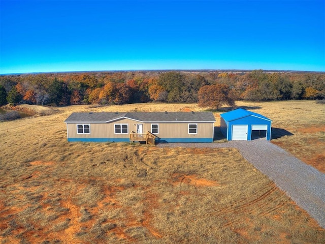 single story home with an outbuilding, a garage, gravel driveway, and a forest view