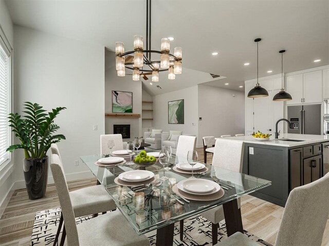 dining area with recessed lighting, a notable chandelier, a glass covered fireplace, and light wood-style flooring