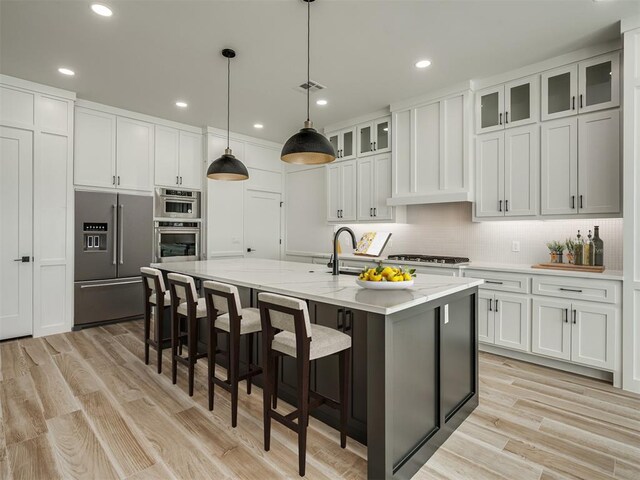 kitchen with a kitchen island with sink, appliances with stainless steel finishes, tasteful backsplash, recessed lighting, and white cabinetry
