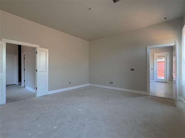 spare room featuring baseboards and unfinished concrete flooring