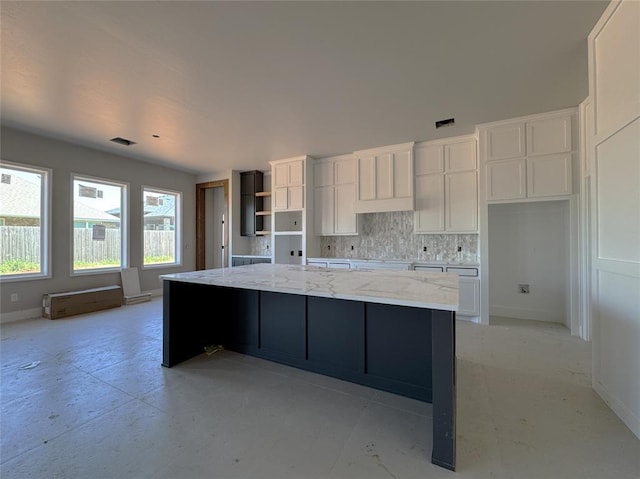kitchen featuring decorative backsplash, a large island, light stone countertops, baseboards, and white cabinets
