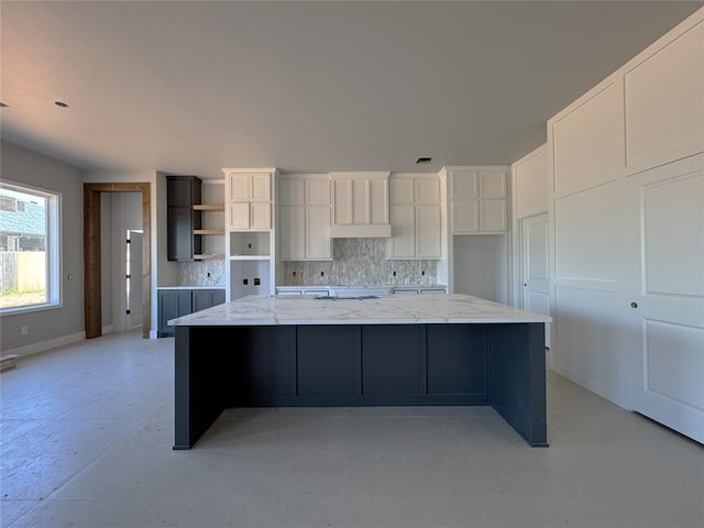 kitchen featuring a large island, white cabinetry, backsplash, and light stone countertops