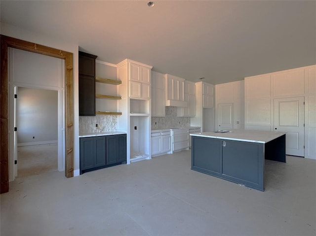 kitchen featuring open shelves, a center island, white cabinets, concrete floors, and backsplash